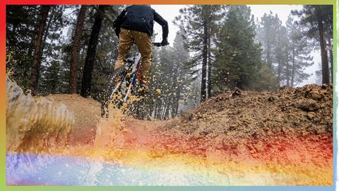 Mountain biker riding through a puddle on a dirt trail with trees surrounding it.